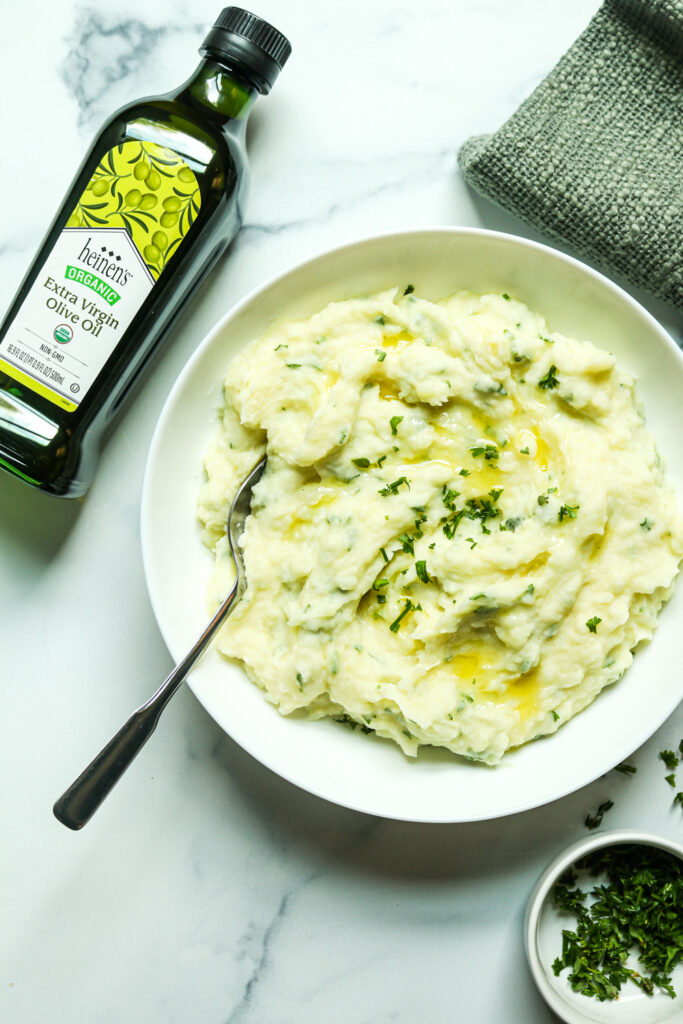 Mashed potatoes in a bowl topped with olive oil and parsley.