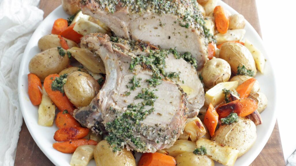 Cooked pork roast topped with herbs over carrots and potatoes.