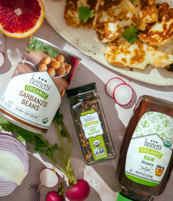 Can of garbanzo beans, jar of Organic crushed red pepper flakes, and a jar of organic raw honey laying on counter.