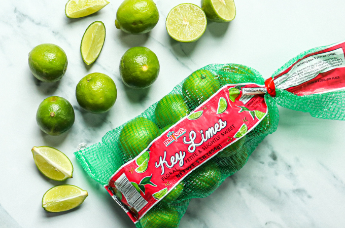 Bag of key limes on a counter surrounded by freshly sliced limes.