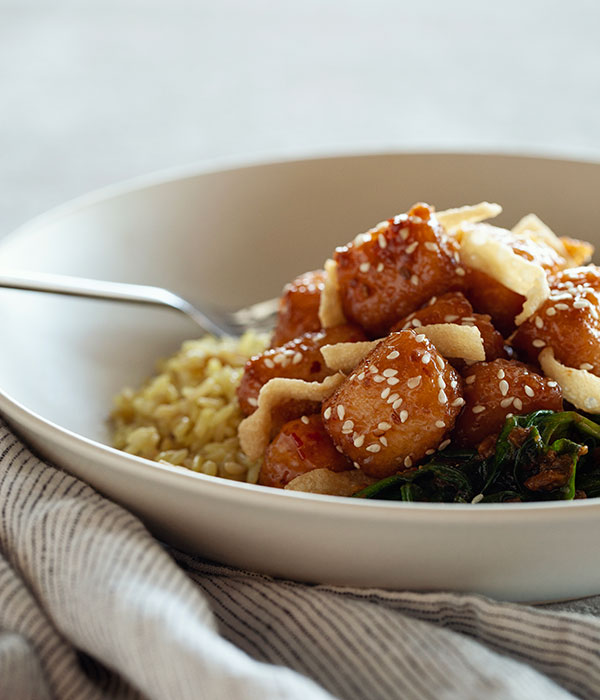 Sweet Chili Tofu with Braised Spinach and Eggplant In a Bowl with a Fork and Napkin