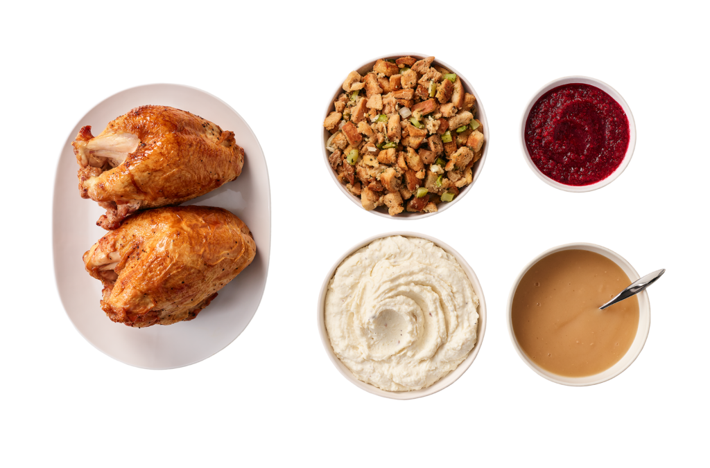 Two Cooked Turkey Breasts on a Plate Beside a Bowl of Crouton Stuffing, a Bowl of Mashed Potatoes, a Small Bowl of Cranberry Relish, and a Bowl of Gravy
