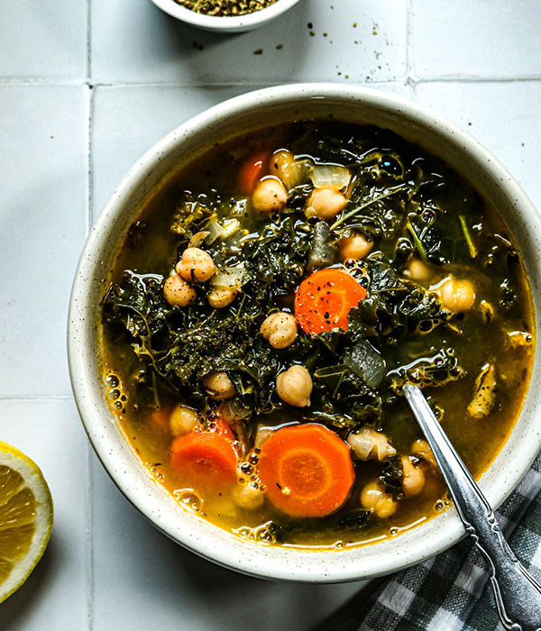 Chickpea soup with carrots and kale in a bowl with a spoon.