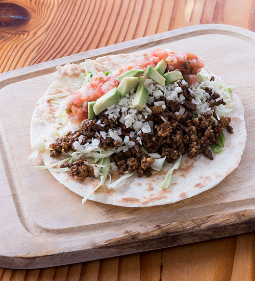 Raw Tao Meat on a Tortilla with Fresh Lettuce and Chopped Tomatoes.