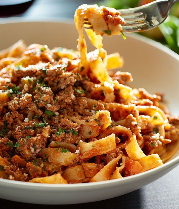 Close Up Vertical Image of Simple Fettuccine Bolognese in a Bowl with a Fork with a Nest of Noodles on It