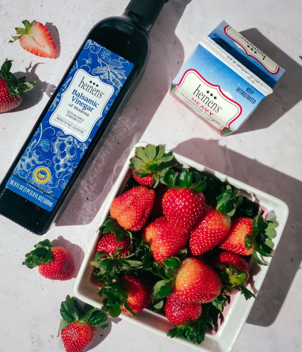 Bottle of Heinen's Balsamic Vinegar, Heinen's Heavy Cream, A bowl of Strawberries sitting on a countertop. 