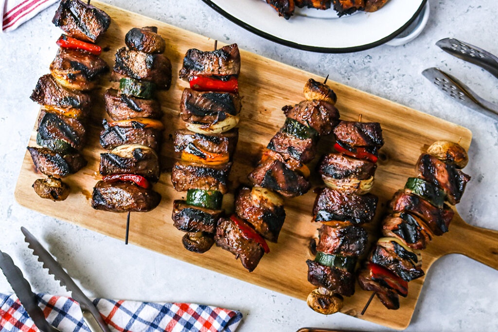 Overhead view of beef and veggie kabobs on a cutting board, placed on a table spread.