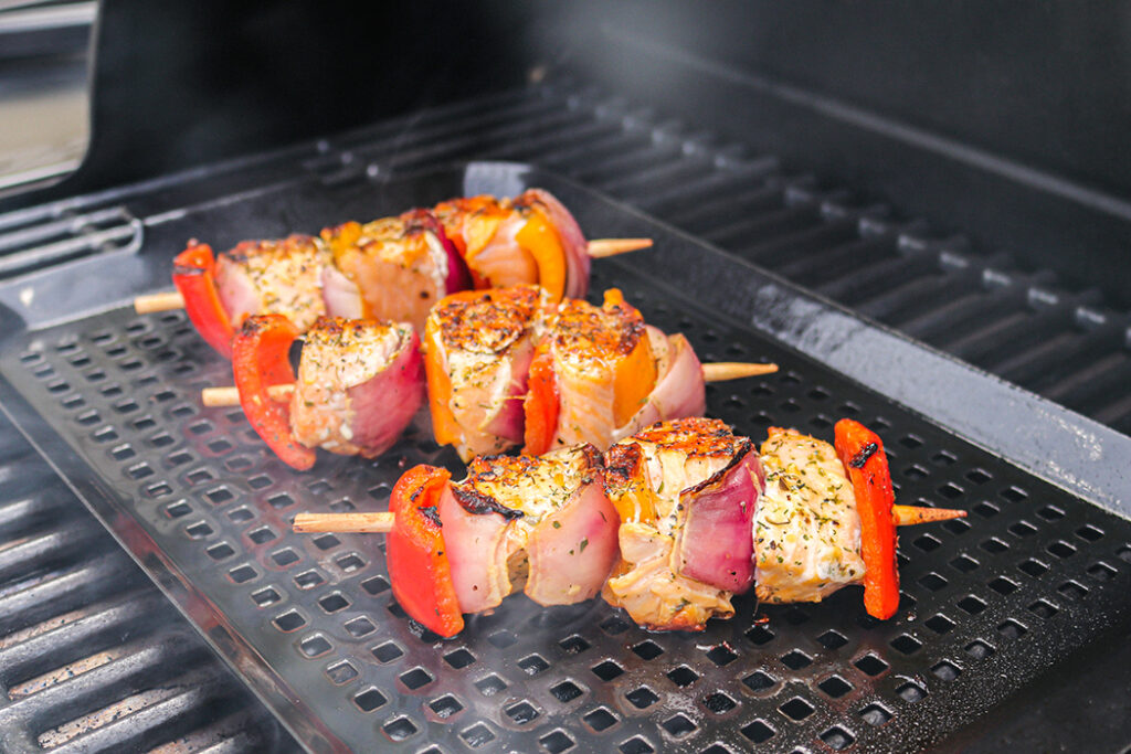Seasoned chicken kabobs with sliced red onion and red bell peppers on a grill.