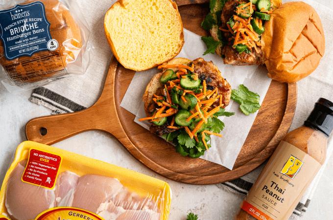 Thai chicken sandwhich with thai peanut sauce, cucumbers, carrots, and leafy greens on a brioche bun.