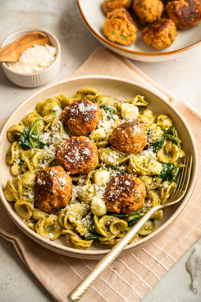 Shell pasta with pesto and meatballs in a bowl, sprinkled with fresh parmesan cheese.
