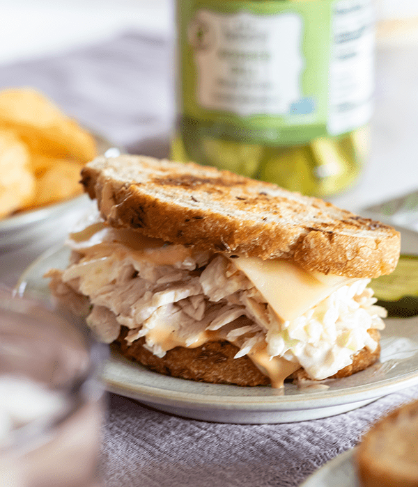 Turkey Rachel Sandwich on a Plate with a Jar of Pickles in the Background