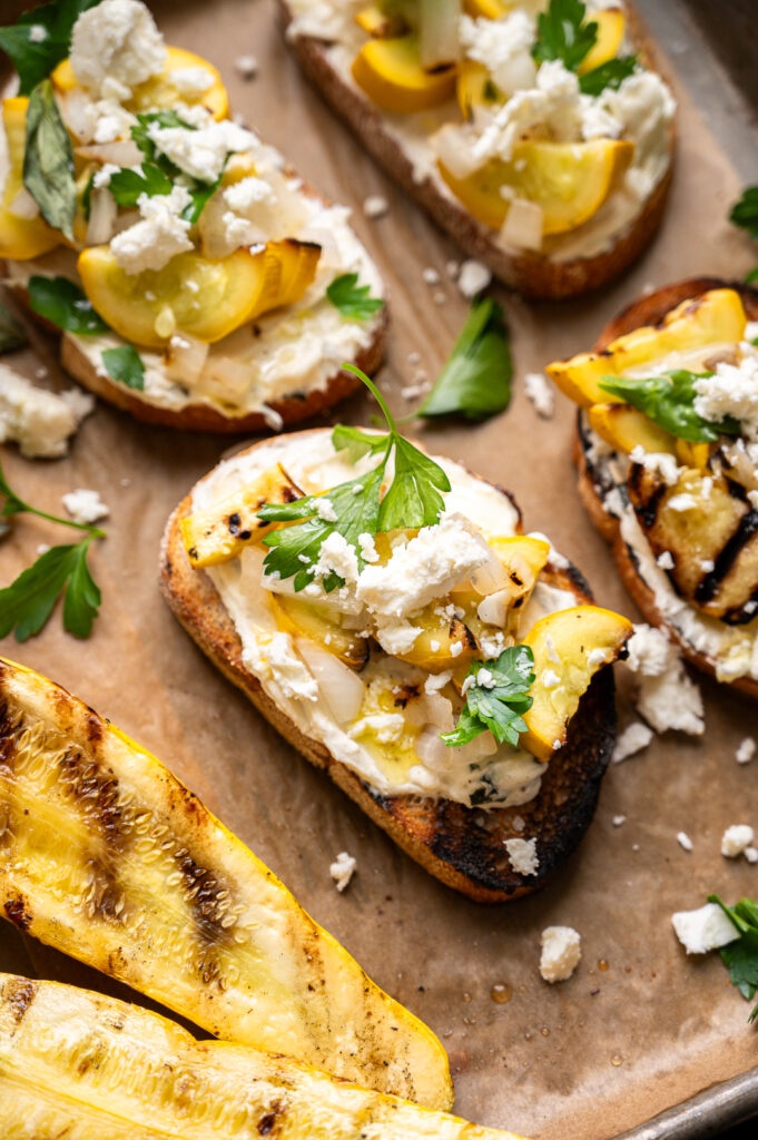 Toast topped with yellow squash and feta arranged on a baking sheet lined with parchment paper.