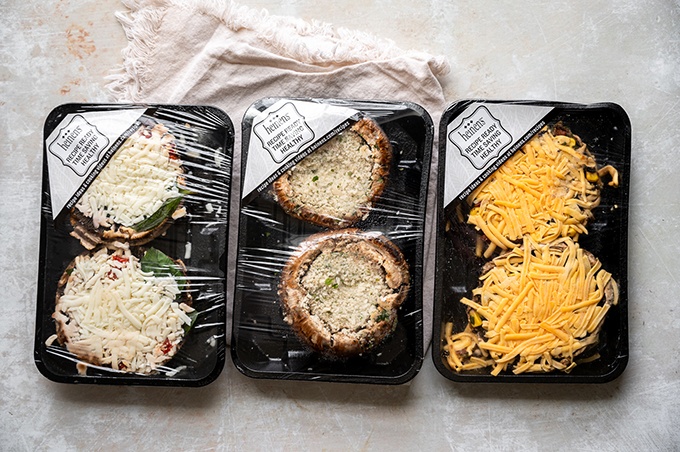 Heinen's caprese stuffed, southwest stuffed, and spinach and artichoke stuffed mushrooms arranged on a kitchen counter.