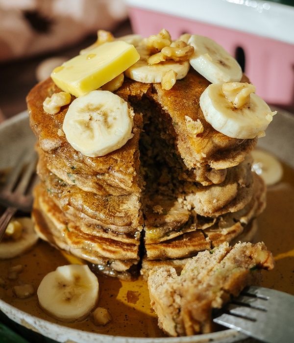 Plate piled high with Zucchini Bread Pancakes topped with butter, bananas, and maple syrup.