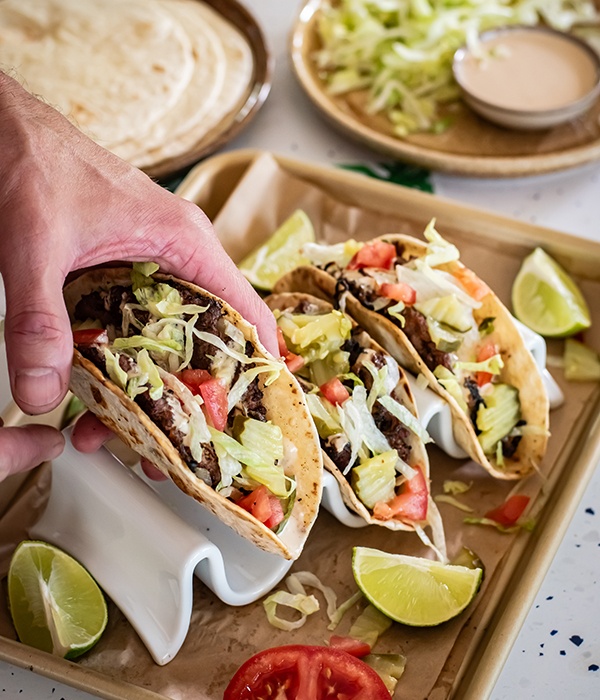 One Smash Burger Taco in hand with two on a tray in the background