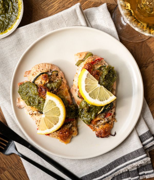Chicken breasts stuffed with sliced squash, tomatoes, and green peppers, topped with pesto and a slice of lemon.