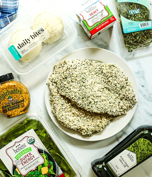 Pork Schnitzel on a plate surrounded by heavy whipping cream, thyme, mixed greens, olive oil, mustard, and mashed potatoes.