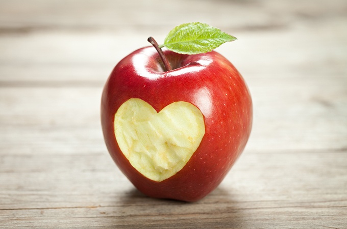 An apple with a heart cut out of the skin on as wooden surface