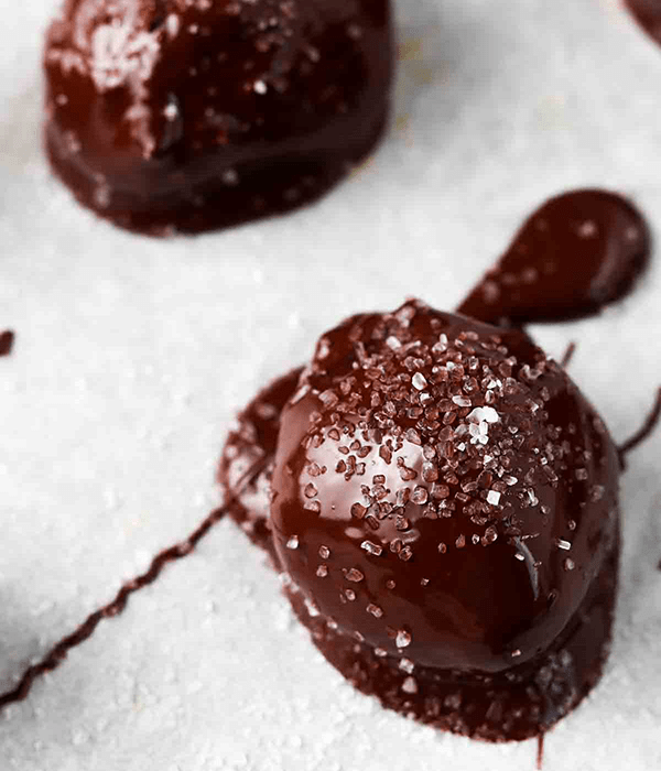Two Chocolate-Dipped Healthy Buckeye Balls on Parchment Paper with a Sea Salt Topping