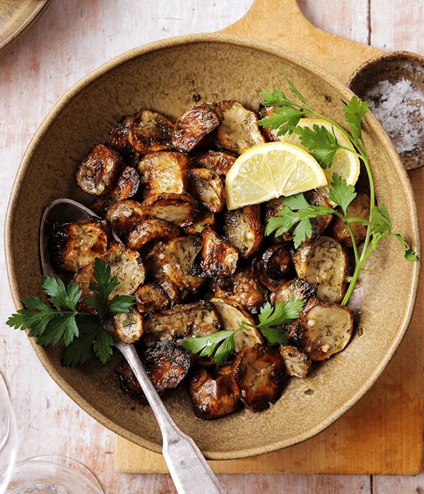 Herby Roasted Sunchoke Salad in a Bowl with a Serving Spoon and Fresh Lemon Wedges