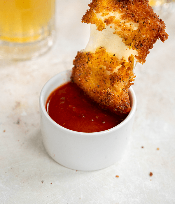 Fried Mozzarella Being Dipped in a Bowl of Marinara Sauce