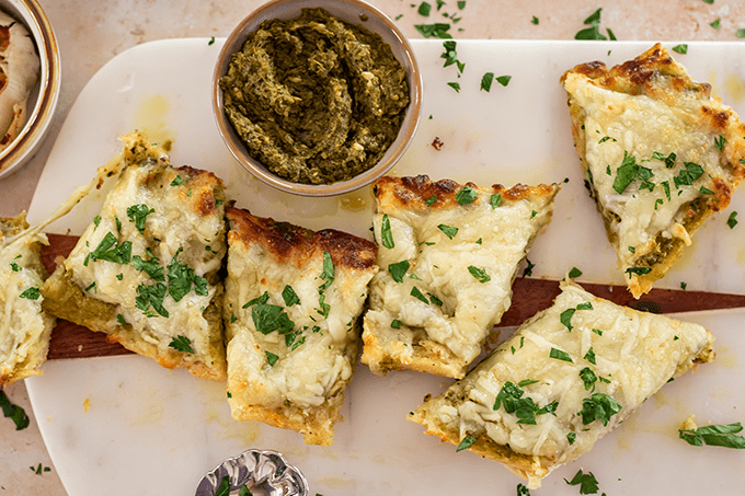 Slice of Cheesy Pesto Garlic Bread topped with parsley on a cutting board.