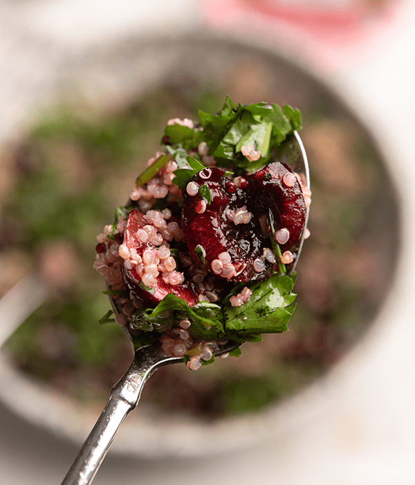 Up close view of a spoon with a cherry, quinoa, mint and parsley salad. 
