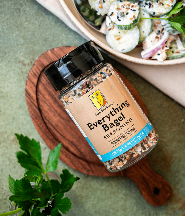Two Brother's everything bagel seasoning sitting on a small cutting board next to an everything bagel cucumber salad. 