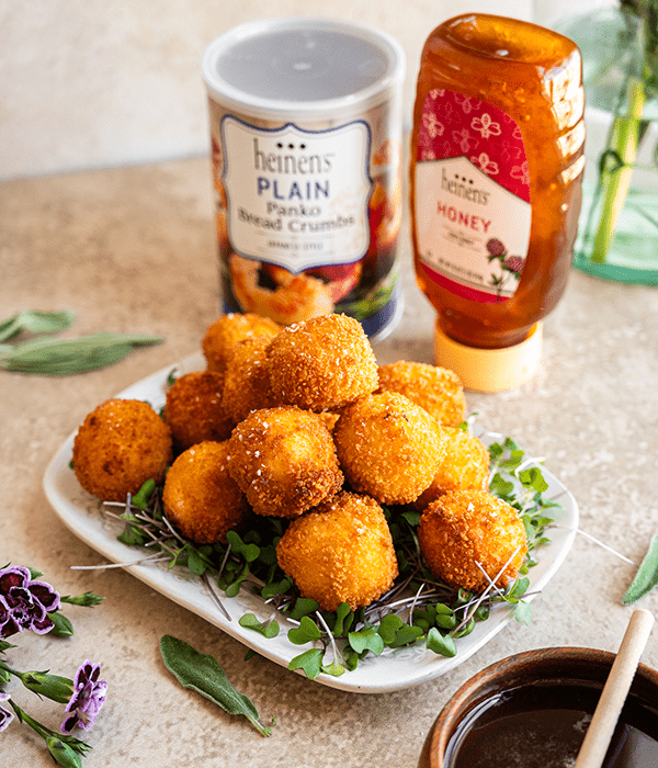 Goat Cheese Balls on a Bed of Microgreens Beside a Container of Panko Bread Crumbs and a Bottle of Honey