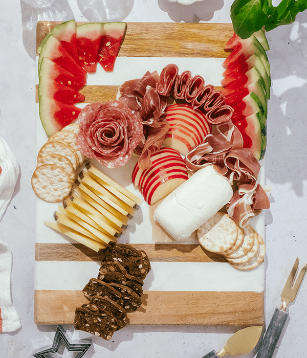 A Partially Assembled Charcuterie Board with Sliced Cheeses, A Whole Goat Cheese Log, Sliced Fruit, and Rolled Charcuterie Meats.