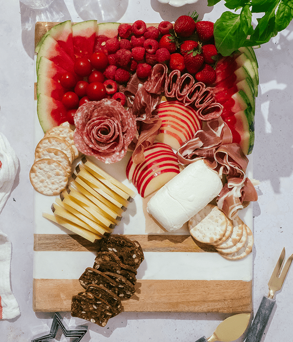 A Partially Assembled Charcuterie Board with Sliced Cheeses, A Whole Goat Cheese Log, Sliced Fruit, Rolled Charcuterie Meats, and Red Berries.