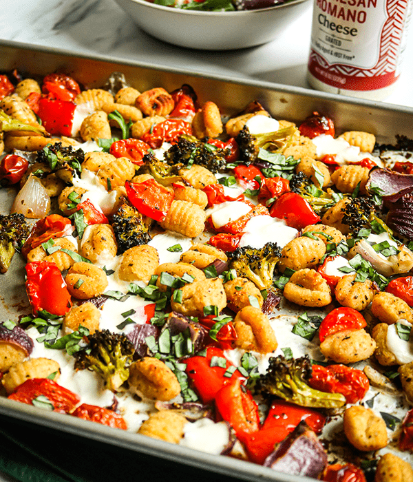 Baking sheet pan lined with parchment paper and topped with potato gnocchi, red bell pepper, onion, and broccoli. 