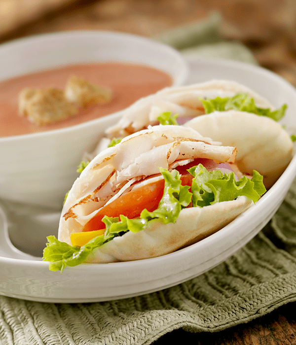 Plate with a turkey pita with tomato and onion and a side of vegetable soup. 