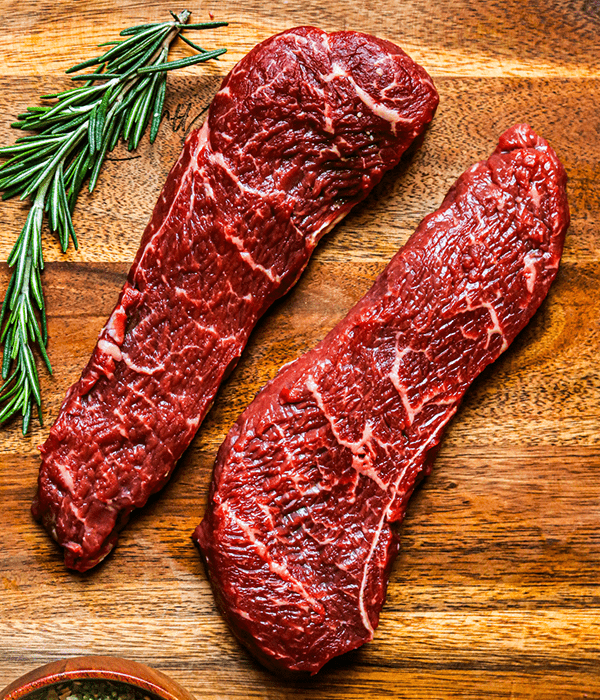 Two Heinen's Premium Raw Coulotte Steaks on a Cutting Board with a Sprig of Rosemary