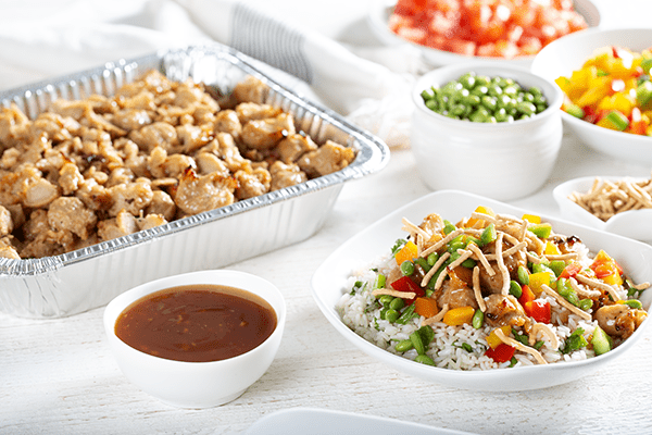 A Vegan Mandarin Nugget Bowl Beside Bowls and Dishes of Cooked Chicken, Sauces, and Chopped Vegetables