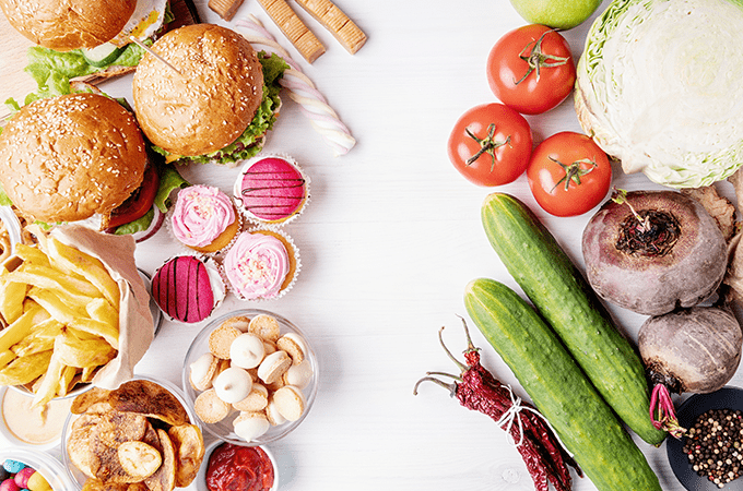 An Assortment of Burgers, Chips and Desserts Beside and Assortment of Fresh Vegetables 