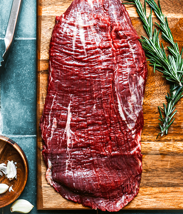 Heinen's Raw Premium Flank Steak on a Cutting Board with a Sprig of Rosemary