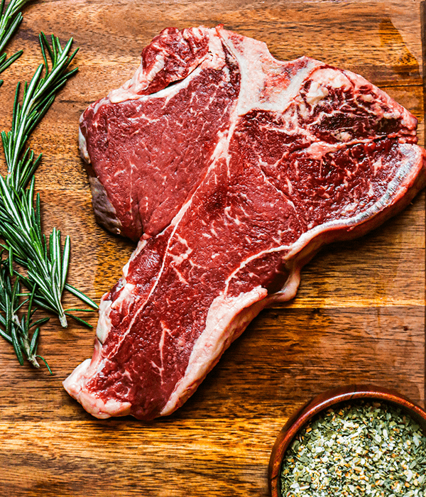 Heinen's Premium Raw Porterhouse Steak on a  Cutting Board with a Sprig of Rosemary