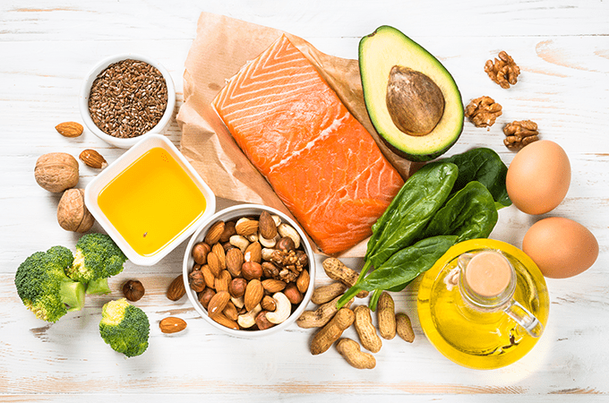 A Top-Down Image of High Fat Foods including Salmon, Avocado, Nuts, Seeds, Oils, and Eggs