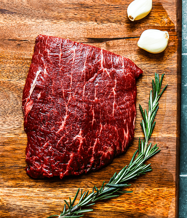 Heinen's Premium Raw Flat Iron Steak on a Cutting Board with a Sprig of Rosemary and Garlic Cloves