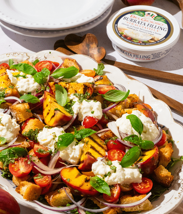 Plate with tomato, peach, and stracciatella salad, and a container of BelGioioso Stracciatella.