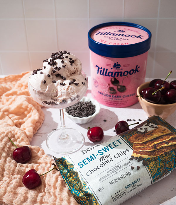 Container of Tillamook Oregon Dark Cherry Ice Cream, bag of Heinne's Mini Chocolate Chips, and sundae with the ice cream and chips