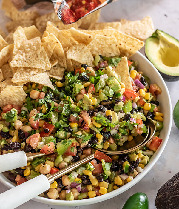 A bowl of cowboy caviar made with avocadoes, cilantro, beans, corn, onions, tomatoes, and served with tortilla chips