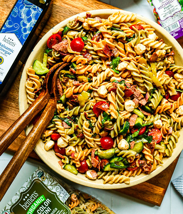 Bowl of Italian Pasta Salad with rotini pasta with tomatoes, cucumbers, onion, mozzarella, salami, pepperoncini, and prosciutto