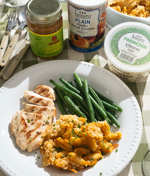 Lemongrass Curry Mac and Cheese plated with chicken and beans, next to a container of grated parmesan, bread crumbs and Red Boat curry