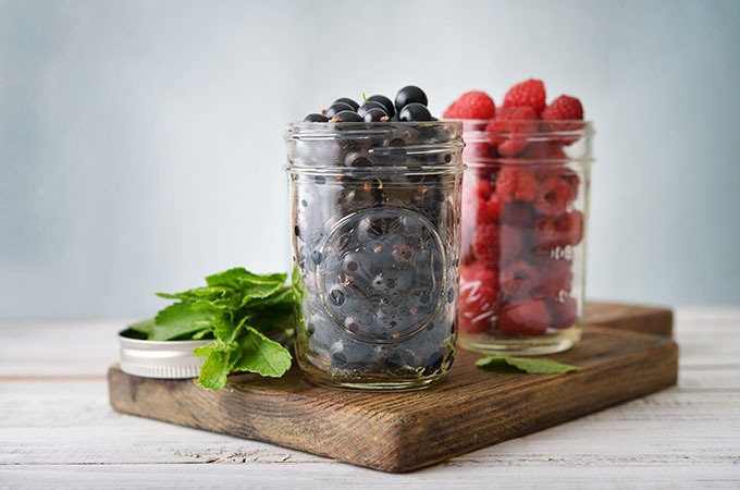 A mason jar full of blueberries and a mason jar full of raspberries