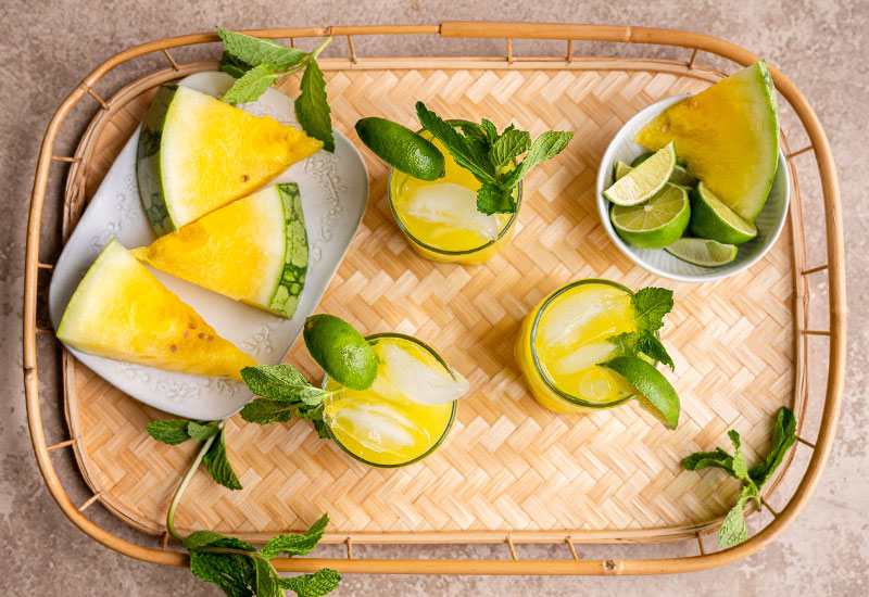 Tray with yellow watermelon and glasses of yellow watermelon fresca garnished with lime and mint