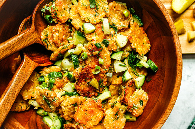 Serving dish of Heinen's Smashed Tater Tot Potato Salad with cucumbers, green onion, and pickles