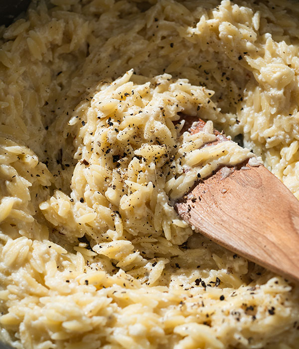 Stirring spoon in dish of creamy orzo pasta
