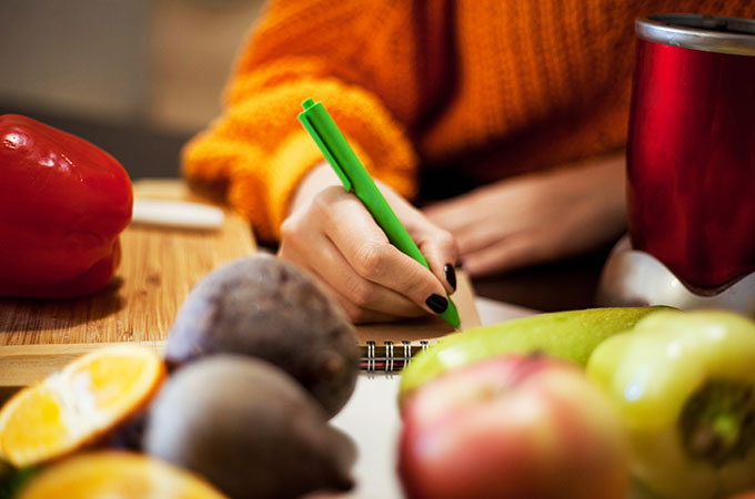 Someone writing on a notepad on a table with fruits and vegetables